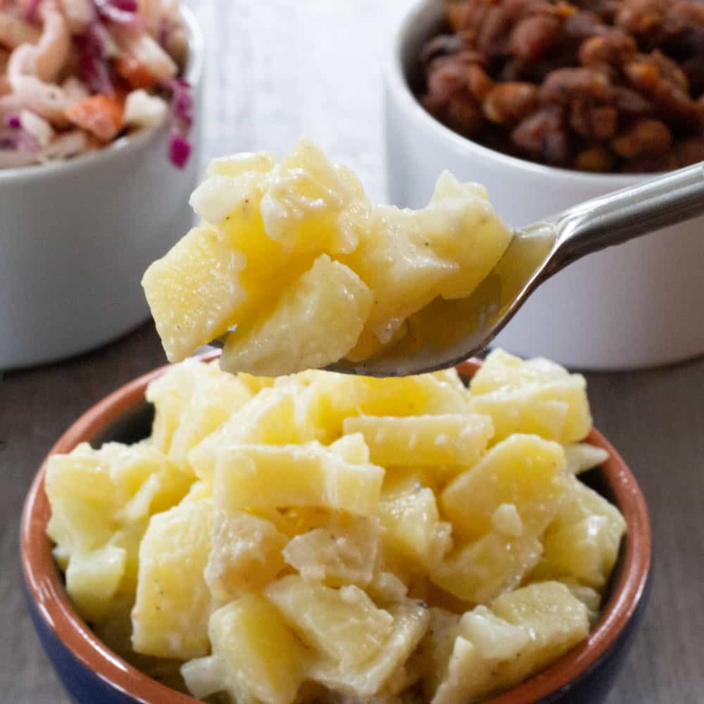 potato salad on fork with cole slaw and baked beans behind