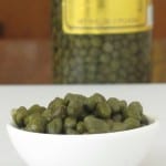 small bowl of capers with big jar of capers in background