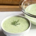 a cup of cucumber avocado soup with a bowl nearby