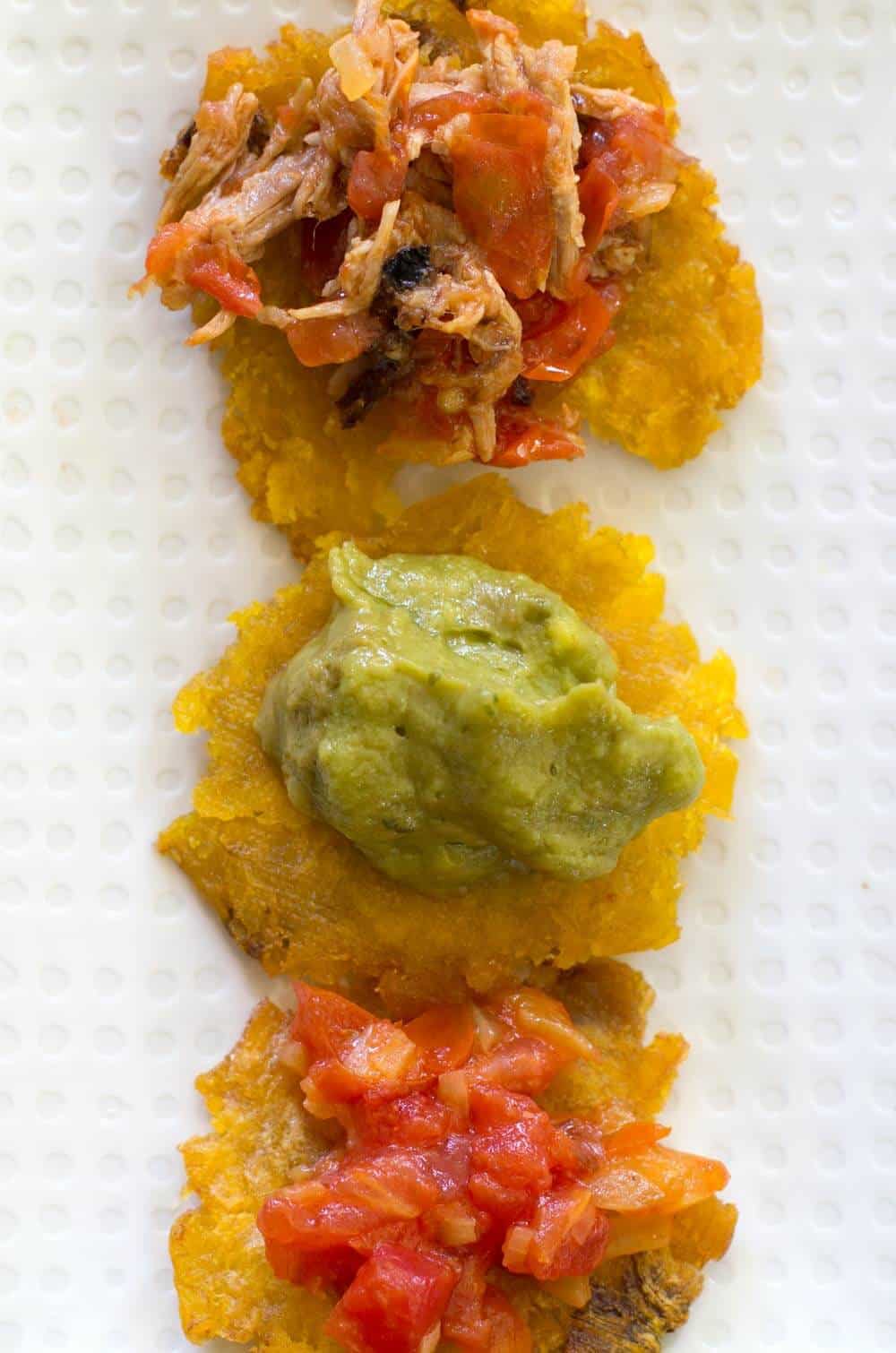 Patacones or green plantains on plate with hogao and other toppings