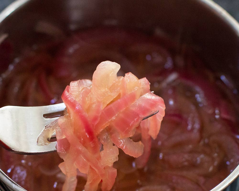 Red onion slices sitting in pickling liquid. 
