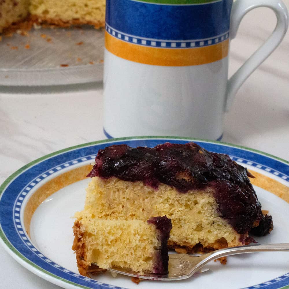 piece of blueberry ginger cornmeal cake with mug of coffee in background