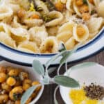 bowl of pasta with chickpeas & sage in back with sprig of sage, chickpeas, lemon zest and pepper in front