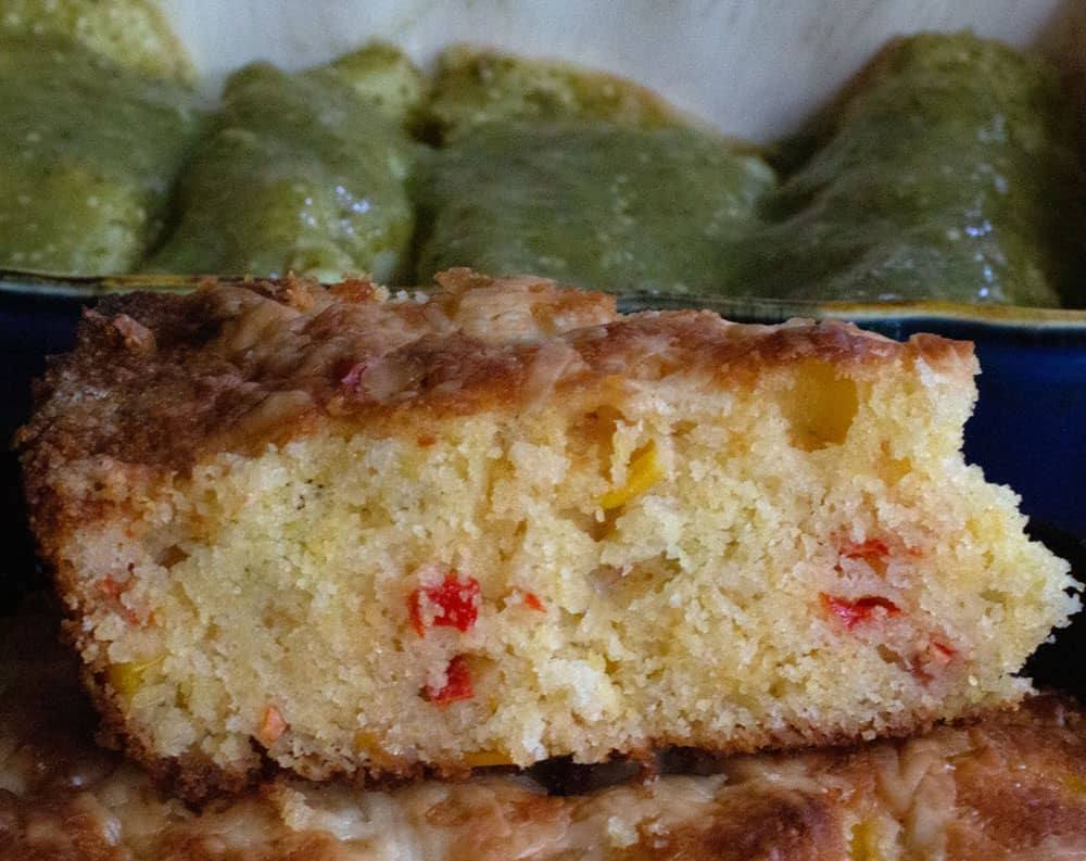piece of loaded cornbread with green sauce-covered enchiladas in background