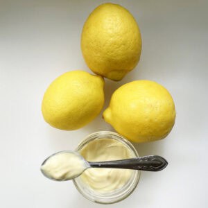 simple and easy lemon curd on a spoon with 3 lemons above in a triangle